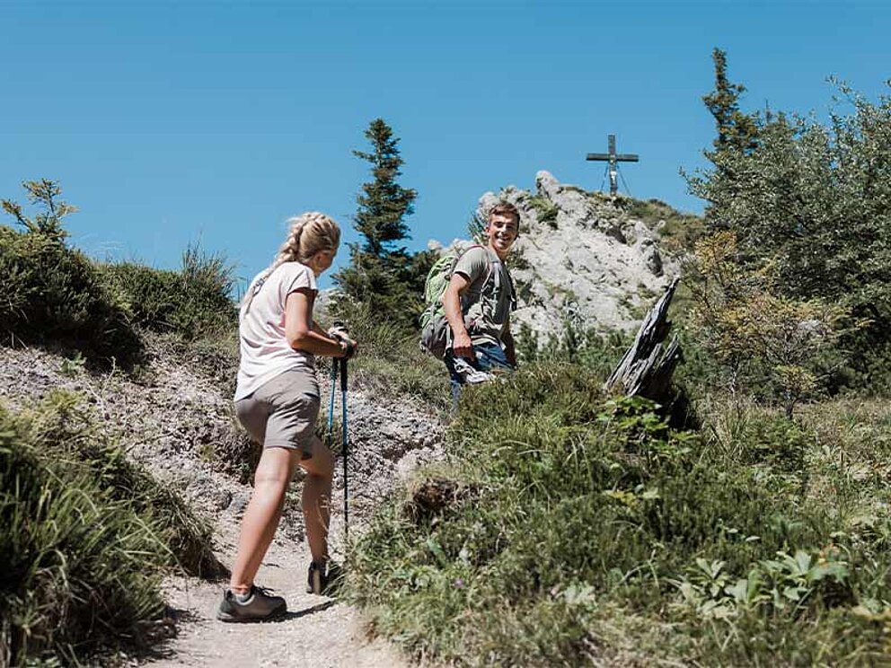 2 Wanderer mit Stöcken am Weg zum Gipfelkreuz im Hintergrund
