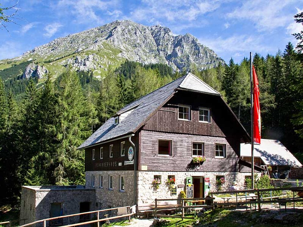 Die Schutzhütte Rohrauerhaus. Davor eine gehisste Österreich Flagge, dahinter der Gipfel des Pyhrgas.