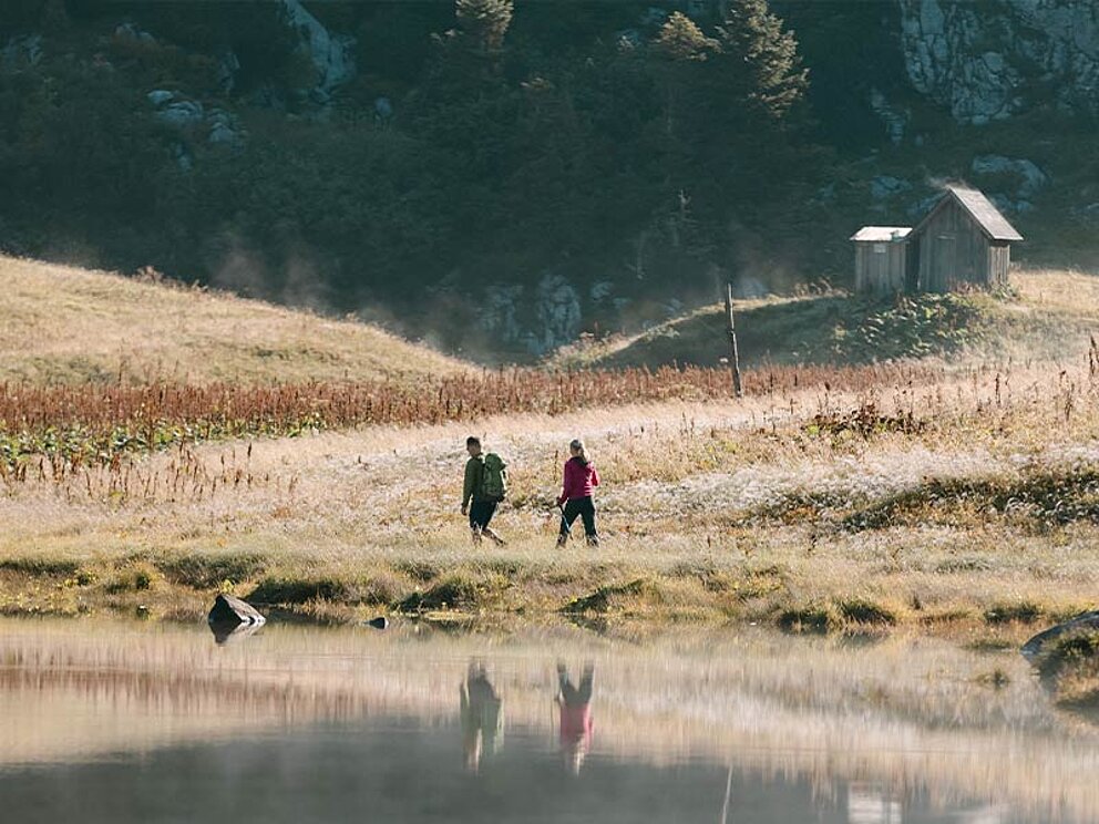 2 Wanderer am Ufer des Elmsees, im Hintergrund eine Hütte