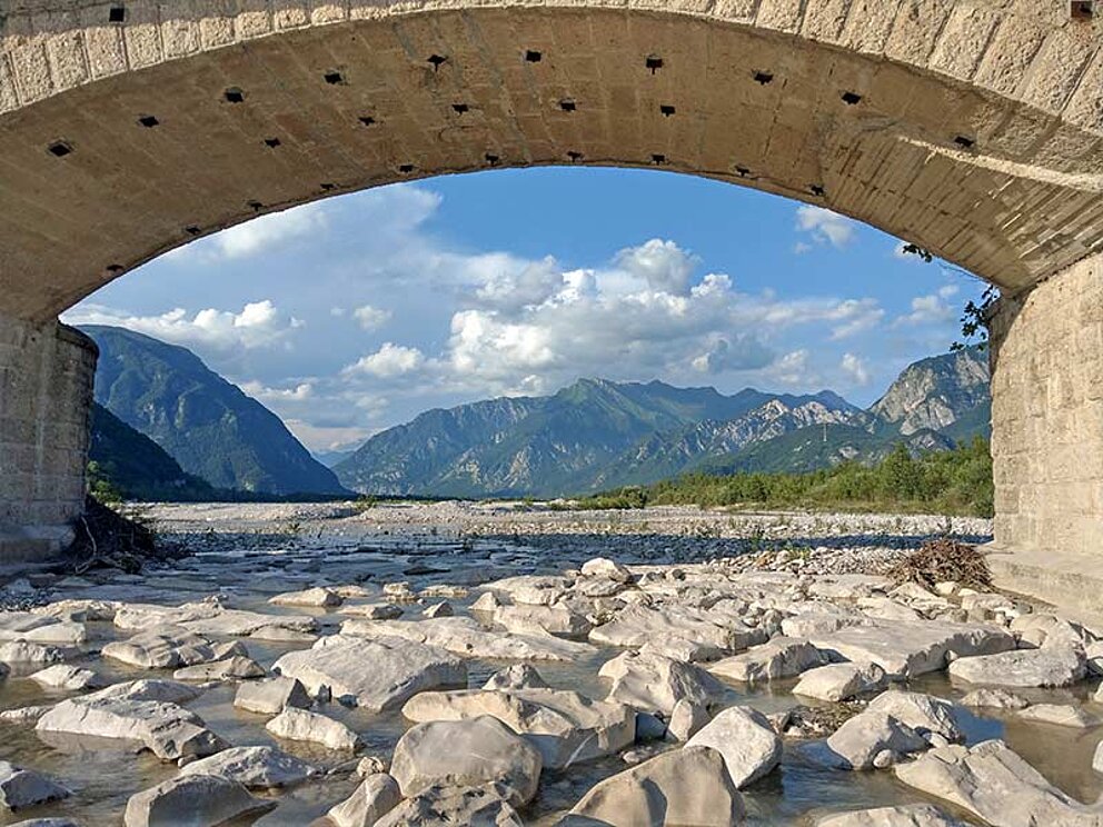 Flussbett mit Steinen, darüber eine Brücke