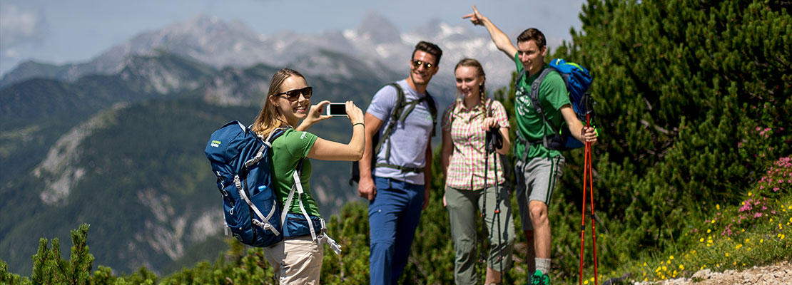 4 Wanderer machen ein Foto mit dem Handy, im Hintergrund Berge